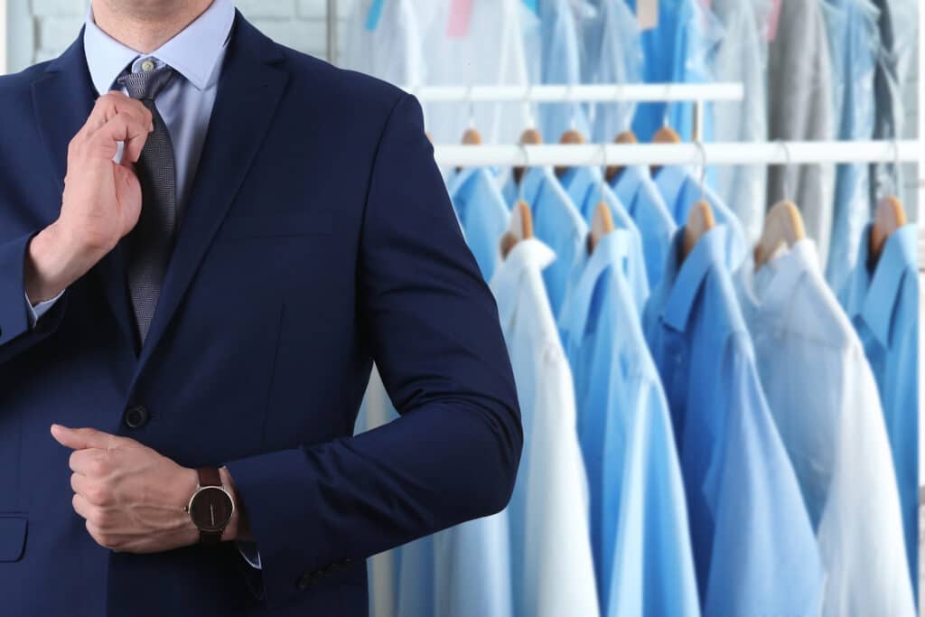 Businessman and rack with clean clothes at dry cleaner's, closeup. Space for text